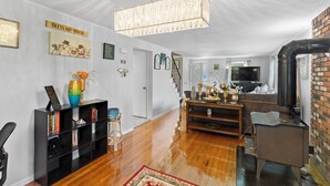 A spacious living room with a wooden floor, a black entertainment unit, a fireplace, and a staircase leading to another level. - Quiet Comfy Getaway 3 BDR home. Close to Bradley Airport. (Windsor)