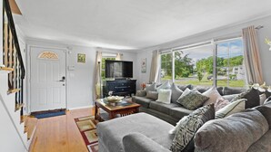 A living room with a sofa, a coffee table, a TV, and a view of the outdoors. - Quiet Comfy Getaway 3 BDR home. Close to Bradley Airport. (Windsor)
