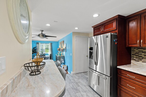 A kitchen with a marble countertop, stainless steel refrigerator, wooden cabinets, and a ceiling fan.