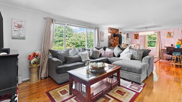 A spacious living room with a grey sofa set, a wooden coffee table, and a large window offering a view of greenery outside. - Quiet Comfy Getaway 3 BDR home. Close to Bradley Airport. (Windsor)