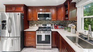 A modern kitchen with stainless steel appliances, wooden cabinets, and a large window. - Quiet Comfy Getaway 3 BDR home. Close to Bradley Airport. (Windsor)