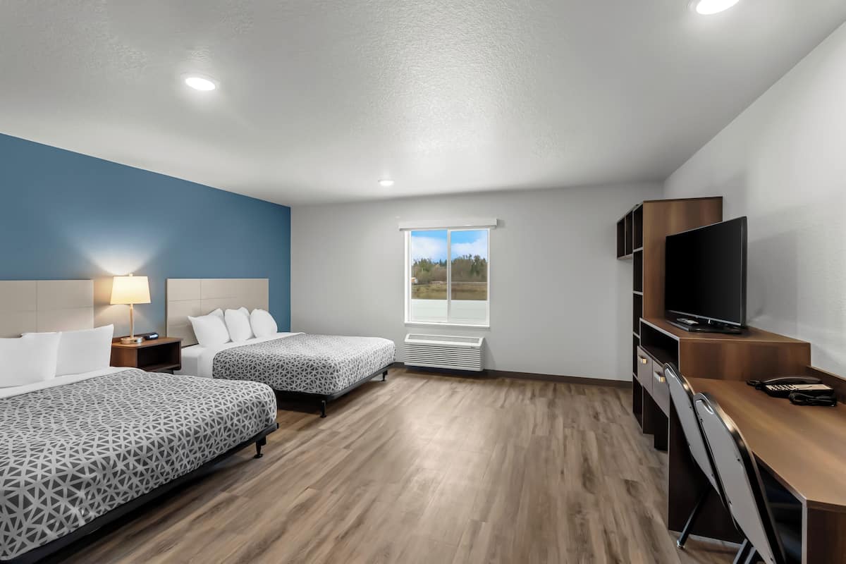 A modern hotel room with two beds, a desk, a television, and a window with a view of the outdoors.