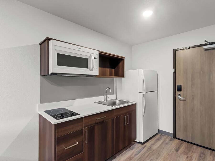 Cocina compacta con microondas, lavabo y refrigerador, armarios de madera y una puerta con picaporte.