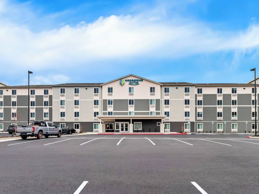 Un hotel Woodspring Suites con estacionamiento y un cielo azul despejado.