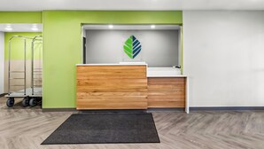 A reception area with a wooden counter, green walls, and a logo on the wall. - WoodSpring Suites Beaverton - Portland West (Beaverton)