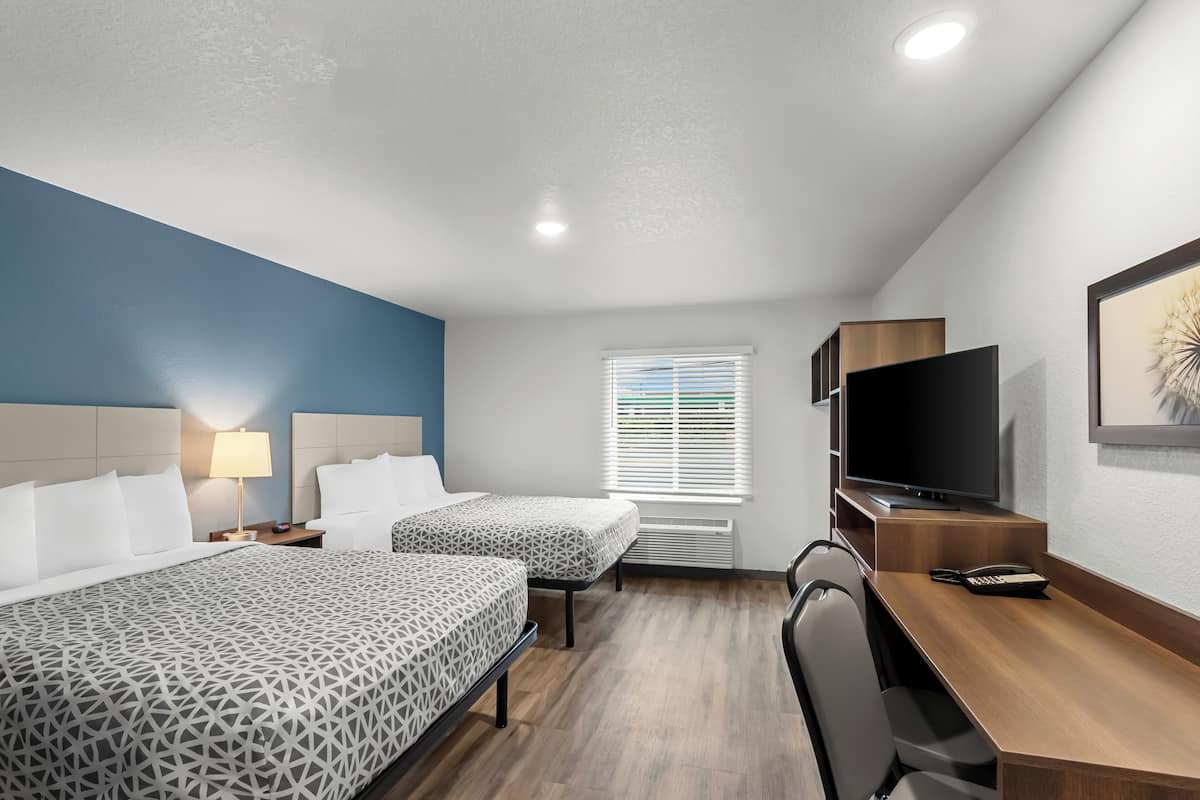 A hotel room with two beds, a desk, a chair, a TV, and a window with blinds.