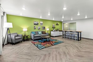 Uma sala de estar moderna com uma parede verde decorativa, um sofá, uma mesa de centro e uma área de jantar com cadeiras.