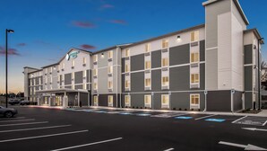 A multi-story hotel with a modern design, featuring a prominent entrance and a parking lot with marked spaces. - WoodSpring Suites Beaverton - Portland West (Beaverton)