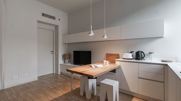 Une cuisine moderne avec des meubles blancs, une table en bois et des luminaires suspendus.