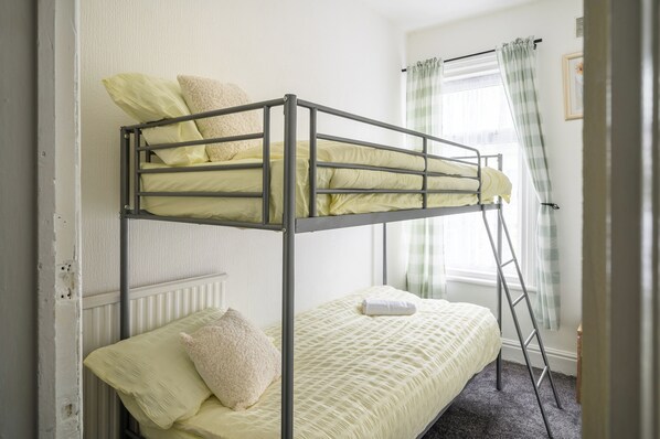 A bunk bed with a ladder, a single bed, and a window with curtains. - Seaside - House - Sleeps 10 - Parking - Garden (Blackpool)