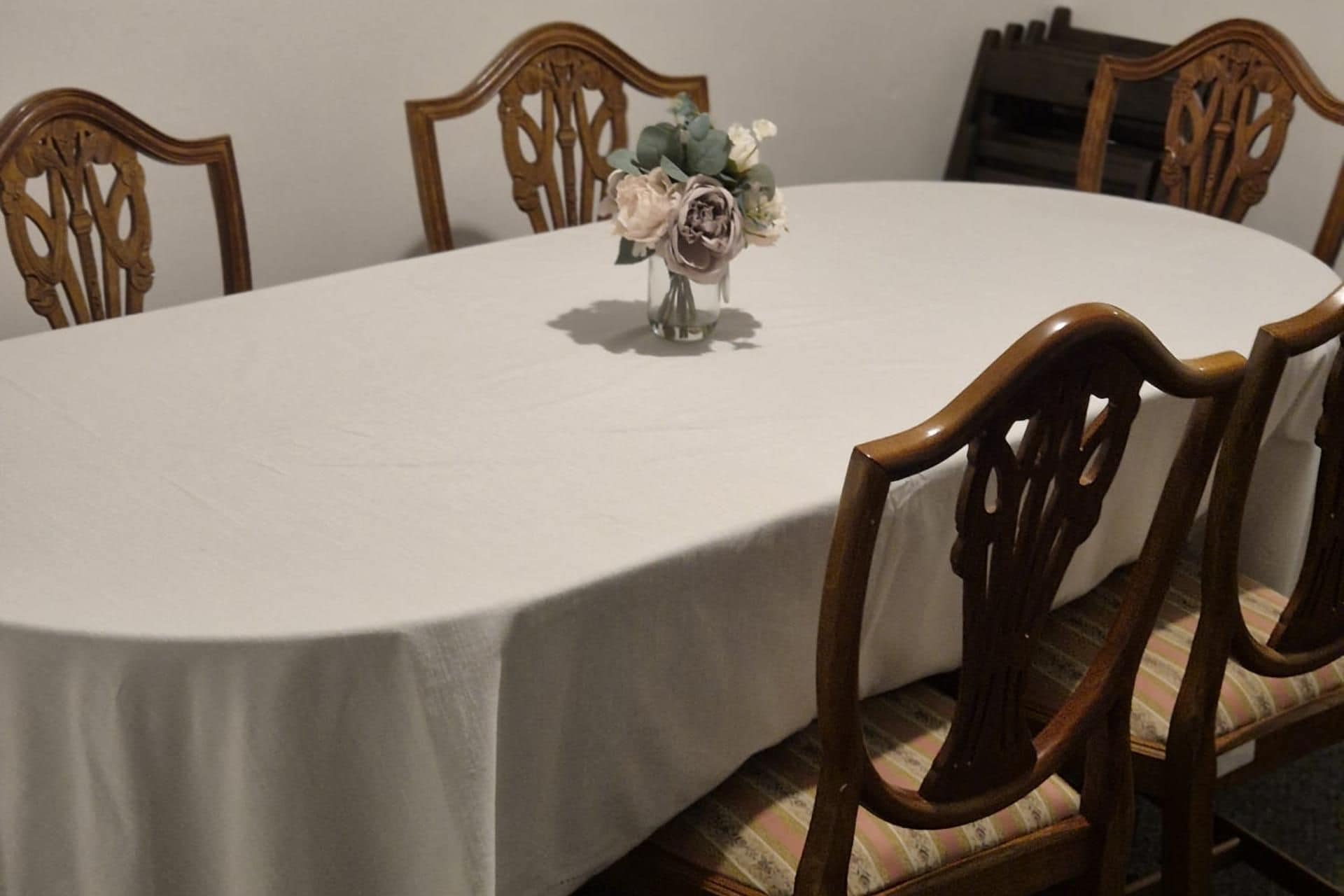 A round dining table with a white tablecloth, surrounded by wooden chairs with cushioned seats.