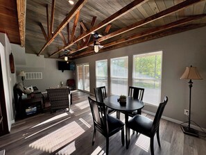 A spacious living area with a dining table, chairs, and a television mounted on the wall. - Chicken Coop Waterfront Cabin on Stocked Pond (Lufkin)