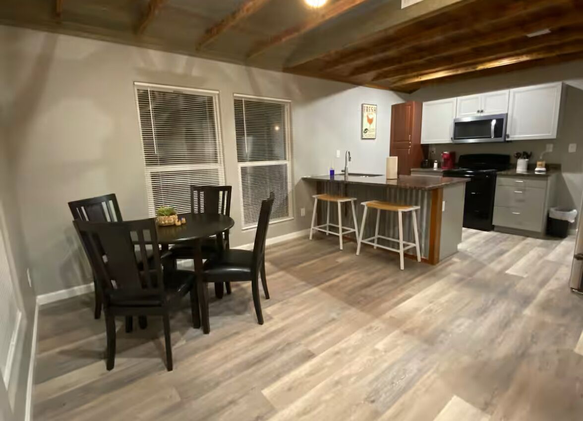 Un comedor con mesa y sillas, una cocina con muebles y electrodomésticos blancos, y piso de madera.