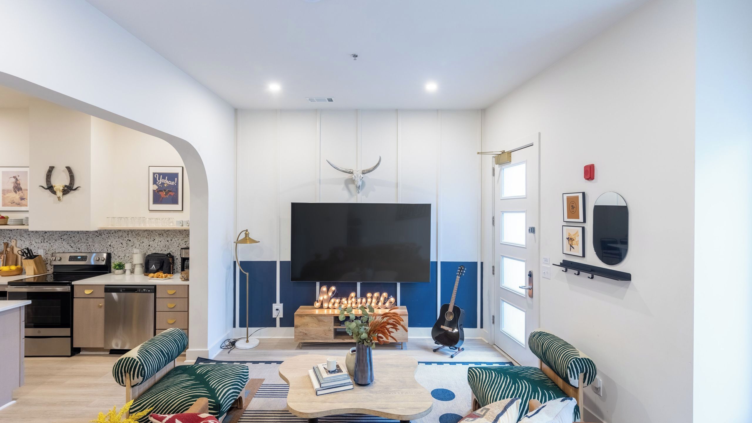 A modern living room with a flat-screen TV, a coffee table, and a seating area with patterned cushions.