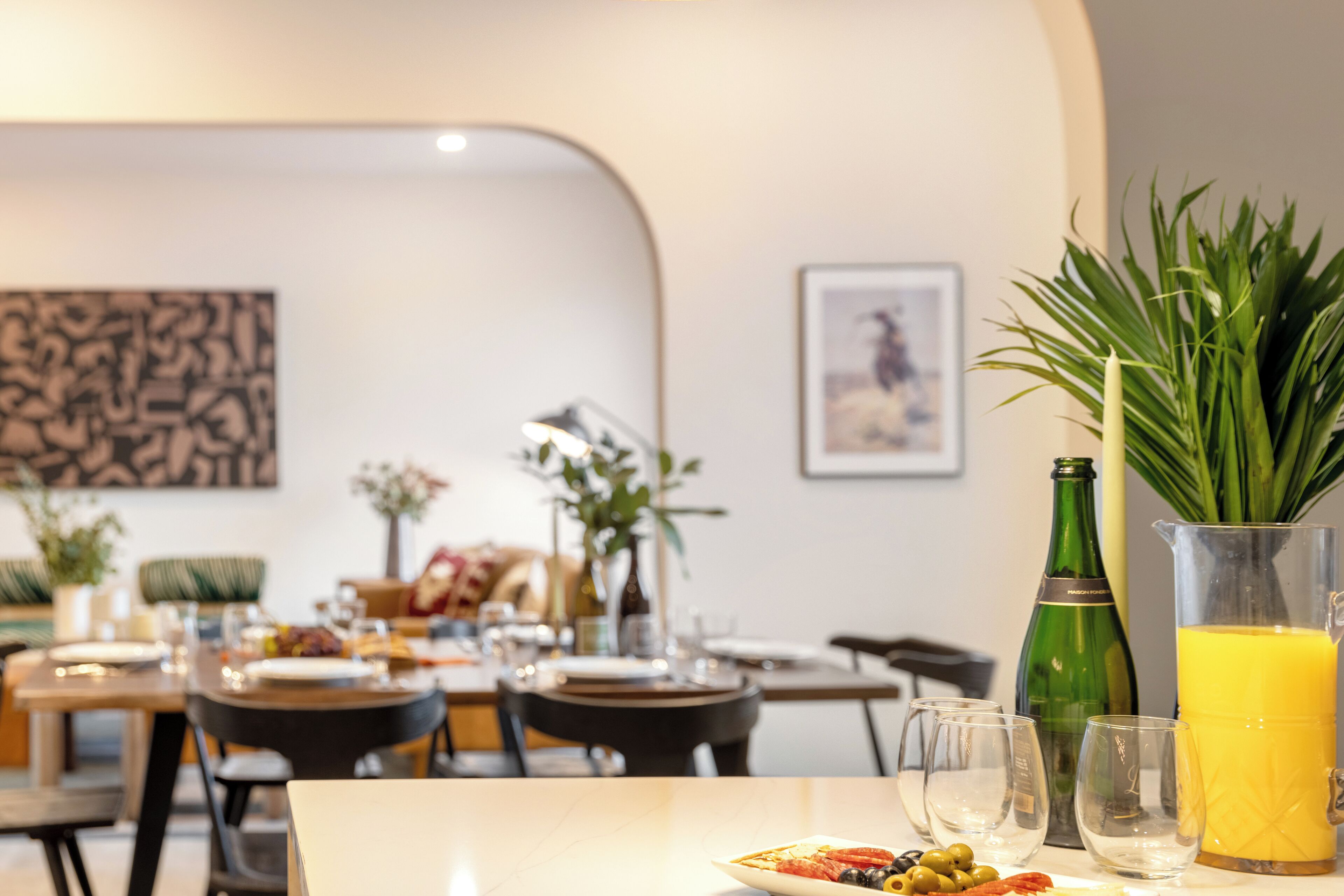 Uma sala de jantar com mesas, cadeiras e diversos tipos de louça, incluindo pratos, copos e uma jarra de suco de laranja.