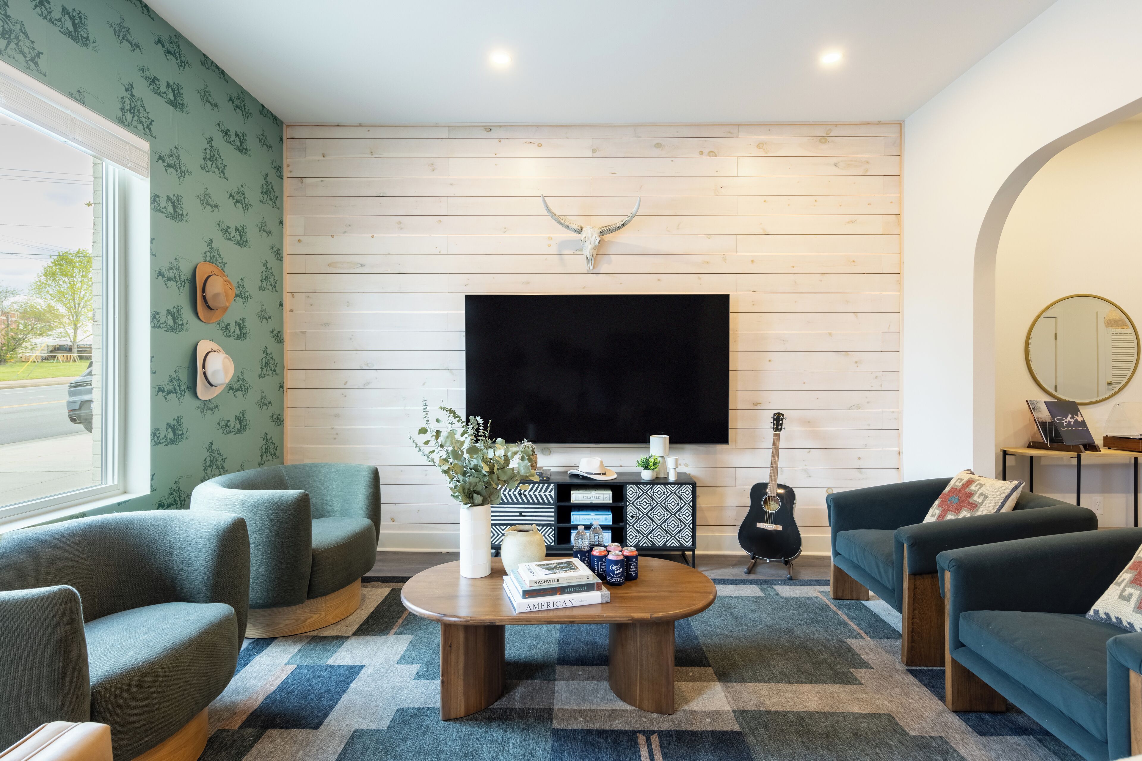 Una sala de estar con un televisor de pantalla plana montado en una pared de madera, una mesa de centro con libros y objetos decorativos, y dos sofás.