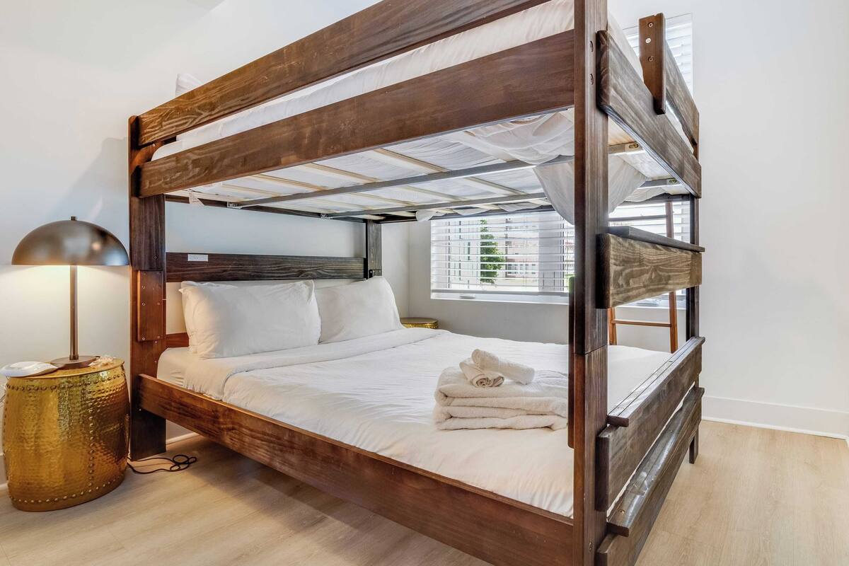 A four-poster bed with a wooden frame and white bedding, a bedside lamp, and a small round table with a golden base.
