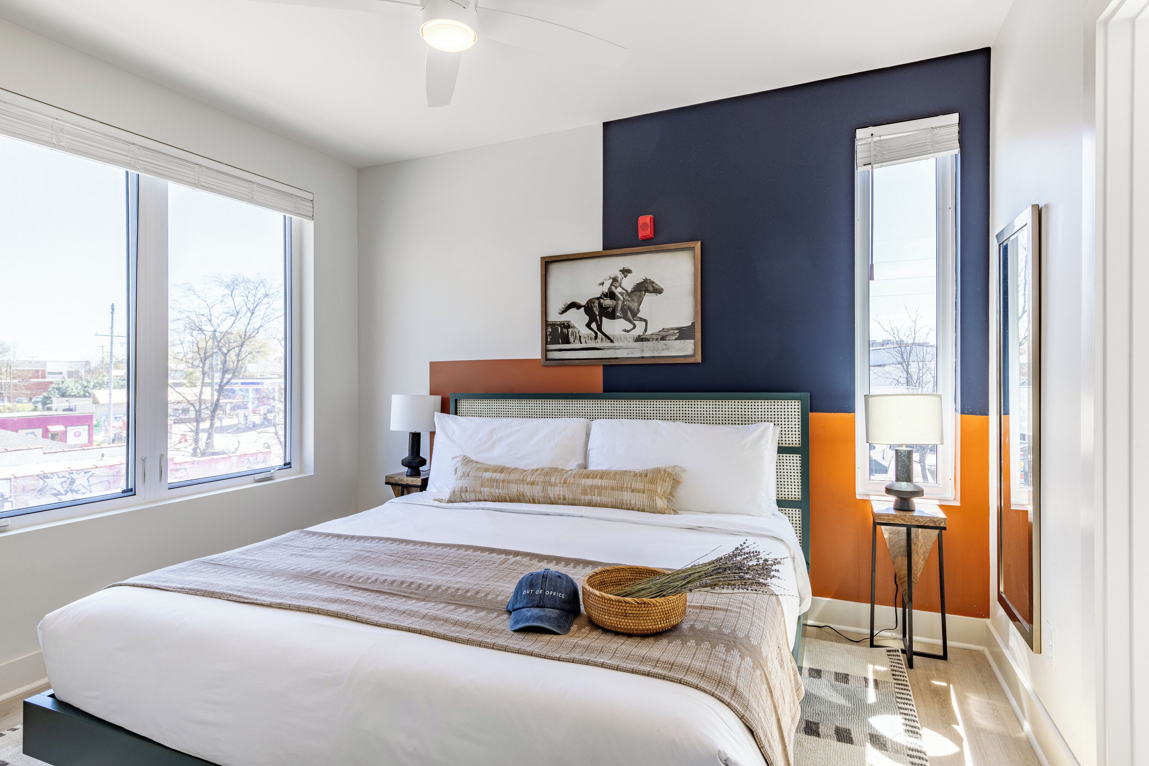 A hotel room with a large bed, a framed picture on the wall, and a view of the city through the windows.