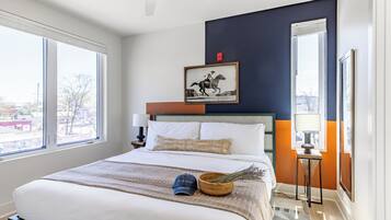 A hotel room with a large bed, a framed picture on the wall, and a view of the city through the windows.