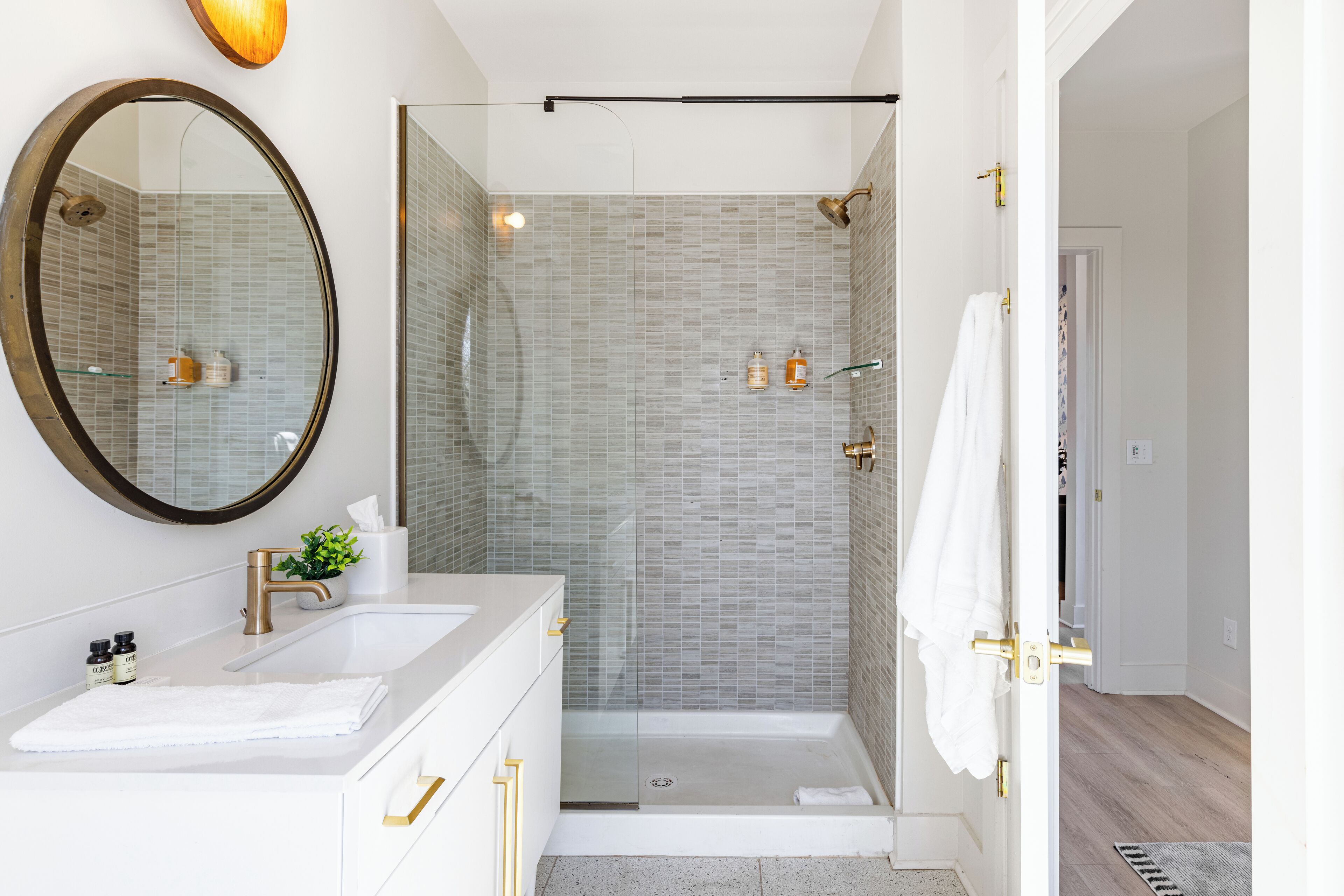 Ein modernes Badezimmer mit einer gläsernen Duschkabine, einem großen Spiegel und einem weißen Waschtisch mit goldenen Armaturen.