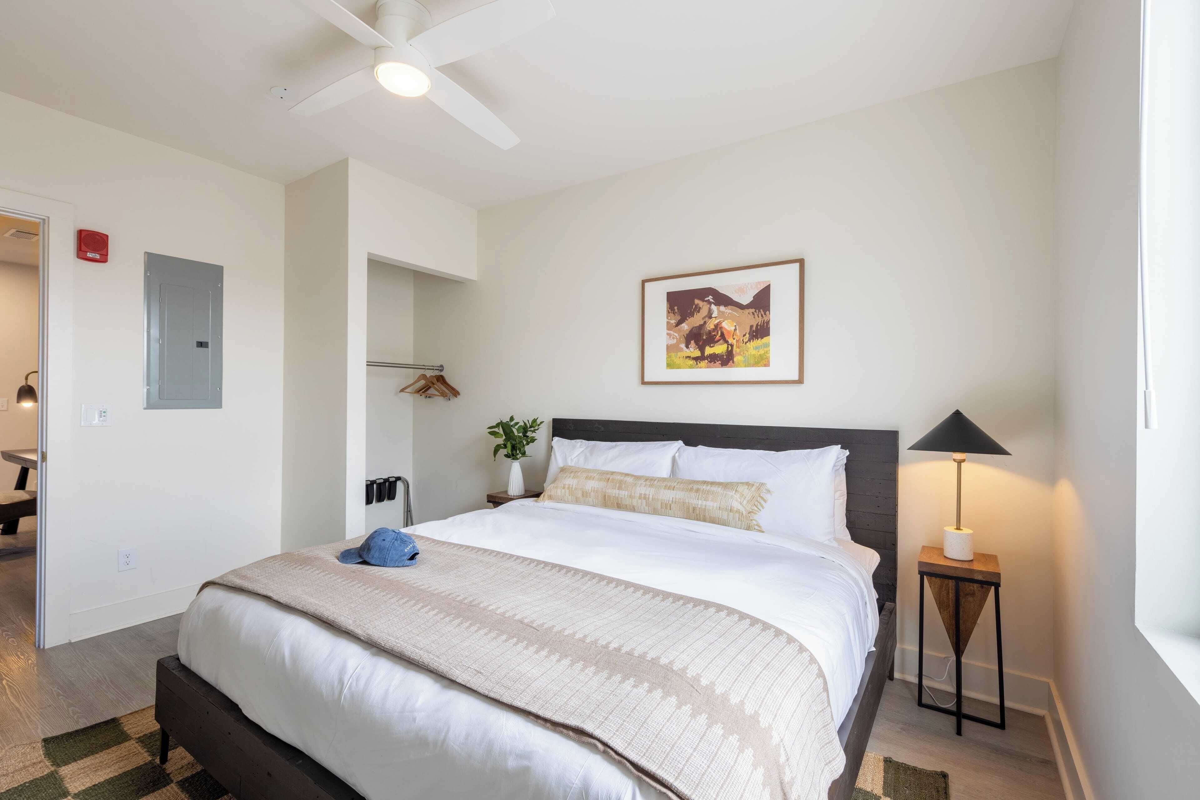 A neatly arranged bedroom with a bed, bedside lamp, and a framed picture on the wall.