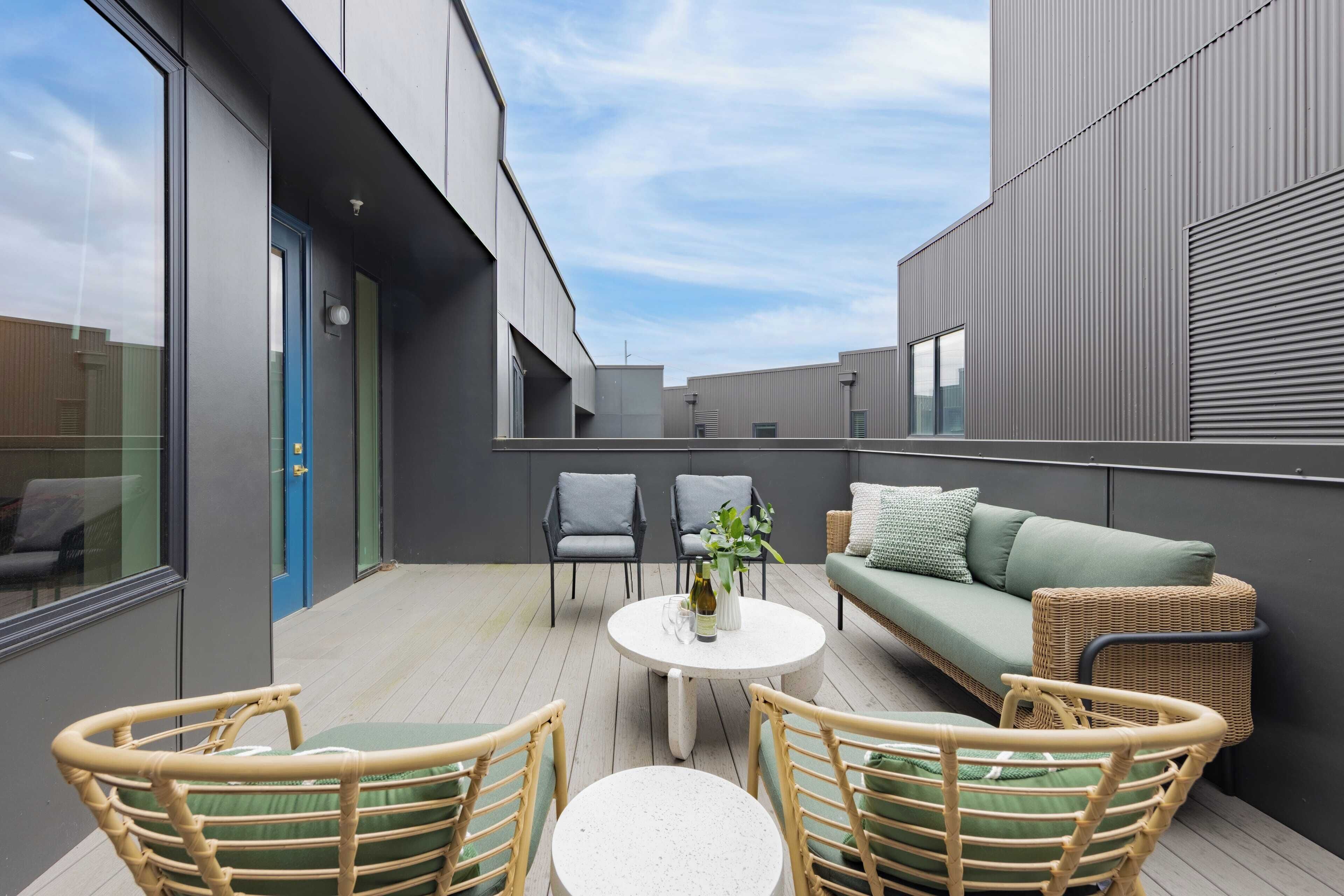 Eine moderne Terrasse im Freien mit einem runden Tisch, Korbstühlen, einem grünen Sofa und einer blauen Tür.
