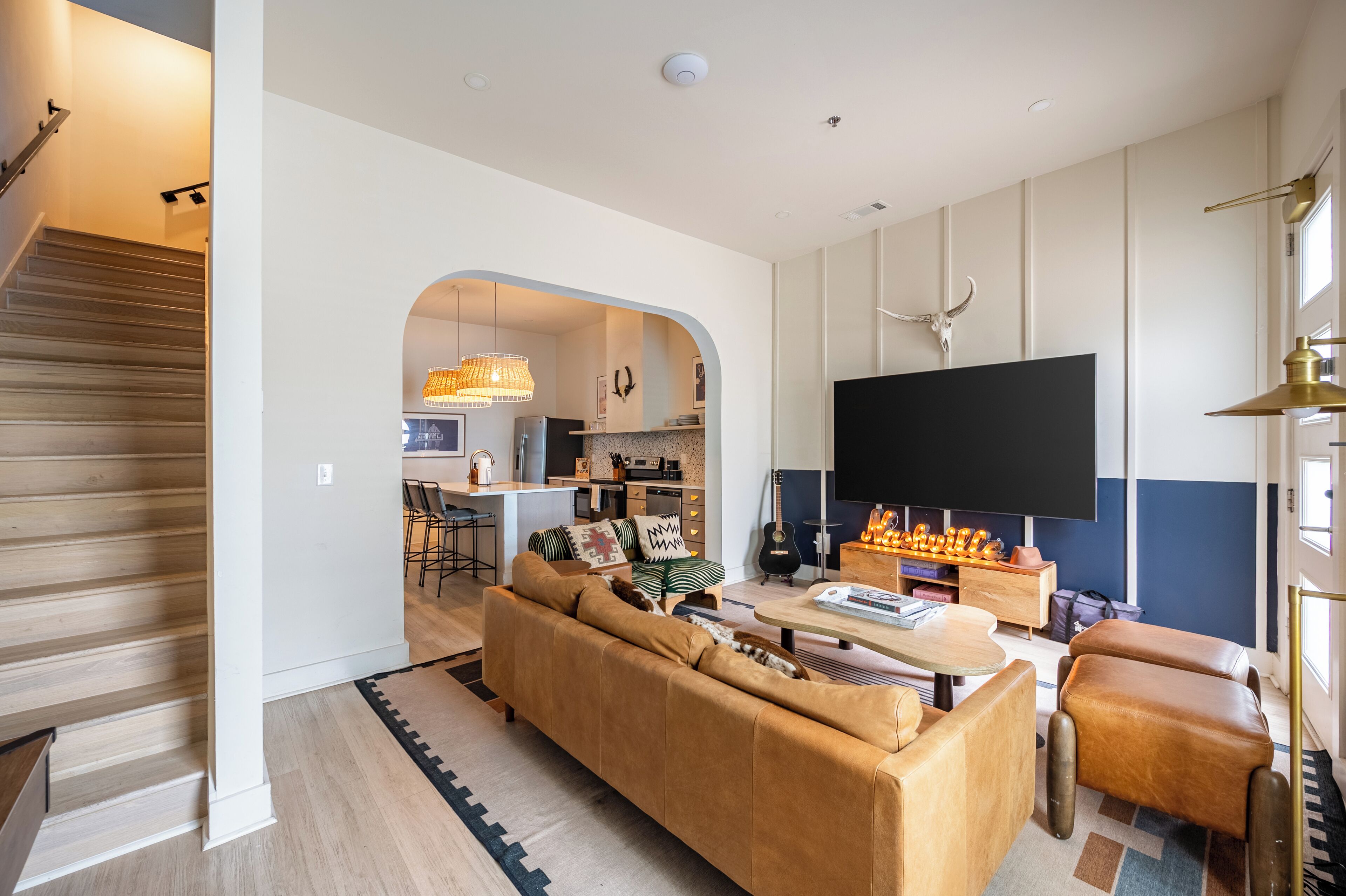 Ein modernes Wohnzimmer mit einer Couch, einem Couchtisch und einem Fernseher. Eine Treppe führt in einen anderen Raum.