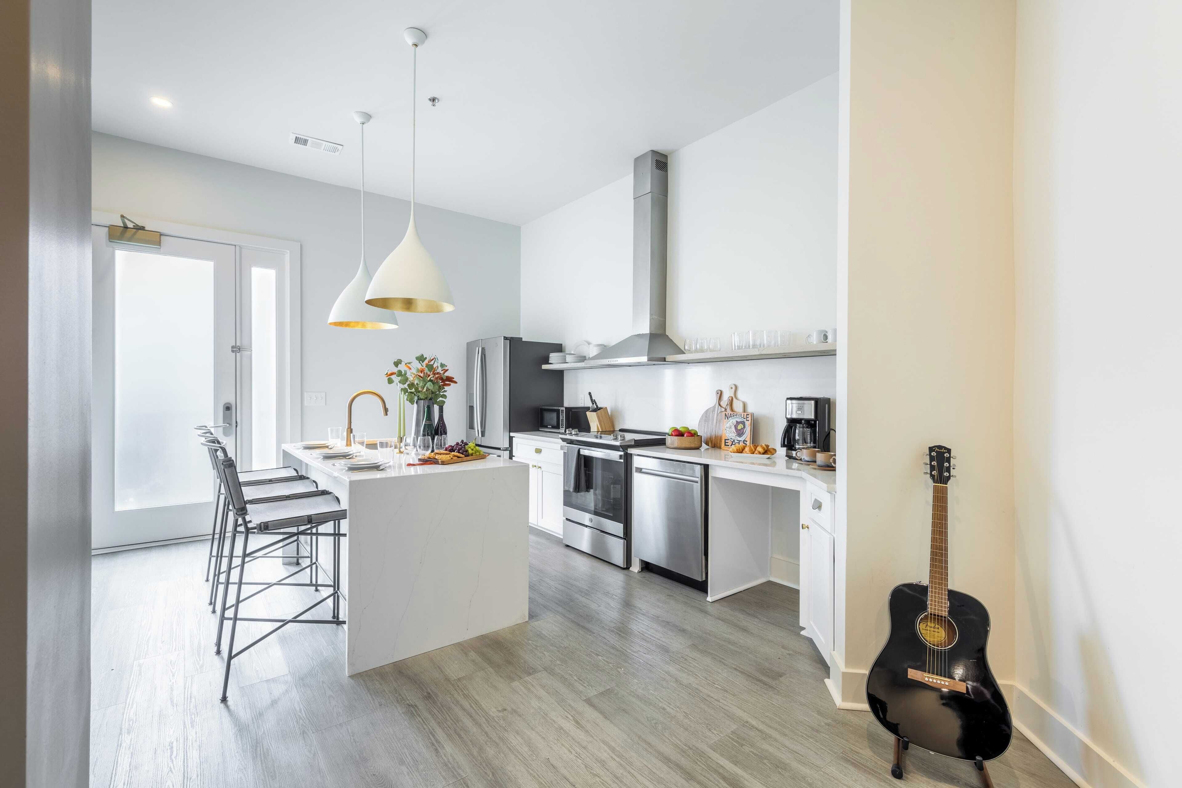 A modern kitchen with a central island, stainless steel appliances, and a black guitar leaning against the wall.
