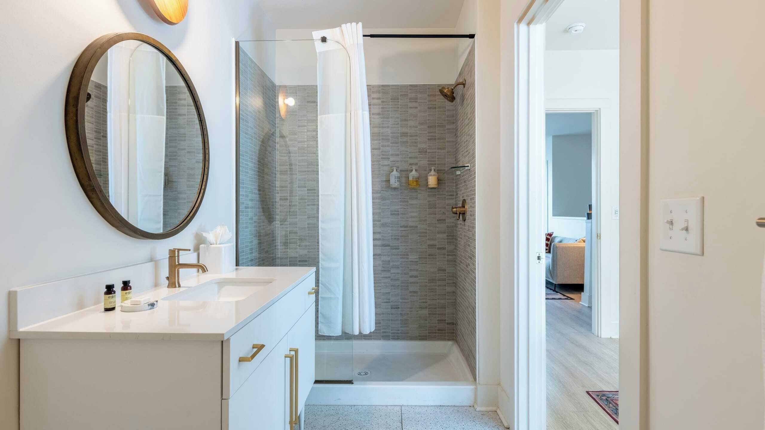 A modern bathroom with a large mirror, a white vanity, and a glass shower enclosure.