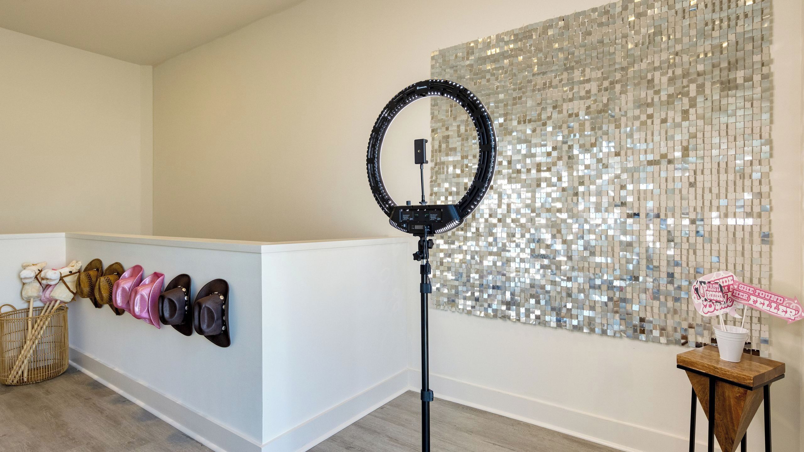 A room with a white reception desk, a ring light, a wall of mirrored tiles, and a small table with a sign.