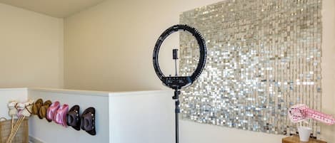 A room with a white reception desk, a ring light, a wall of mirrored tiles, and a small table with a sign.