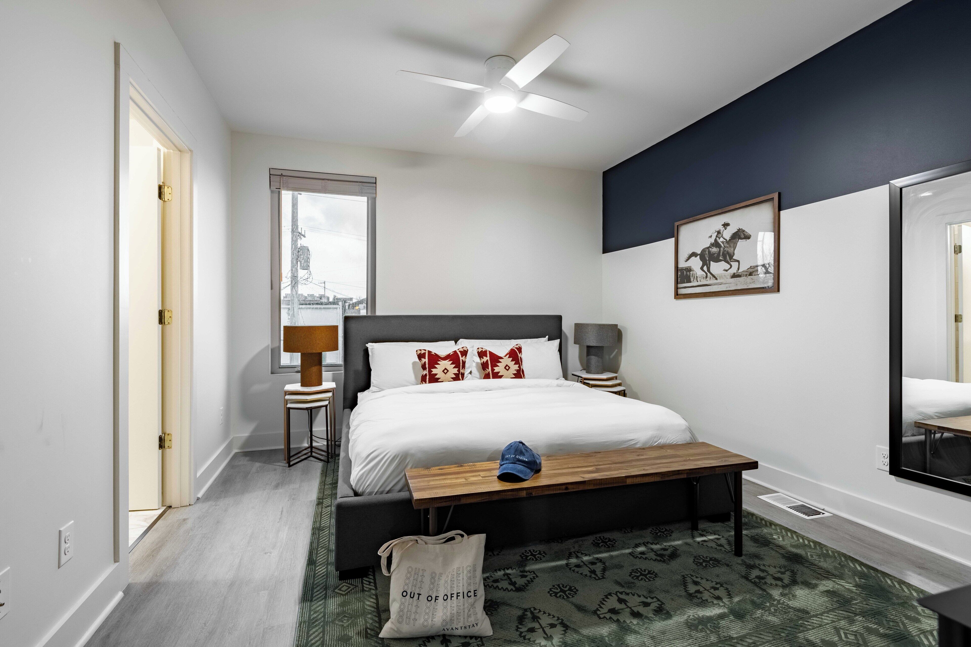 Une chambre d’hôtel moderne, dotée d’un grand lit, d’un bureau, d’une chaise, d’une lampe, d’une fenêtre et d’un miroir.