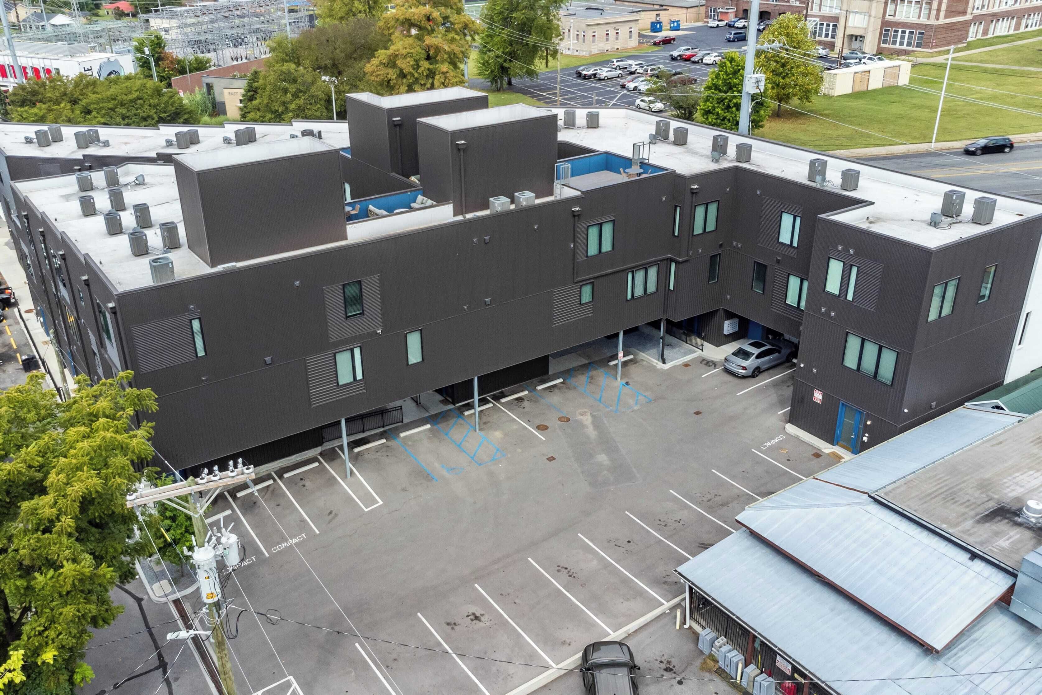 A multi-story building with a flat roof, air conditioning units, and a parking lot.