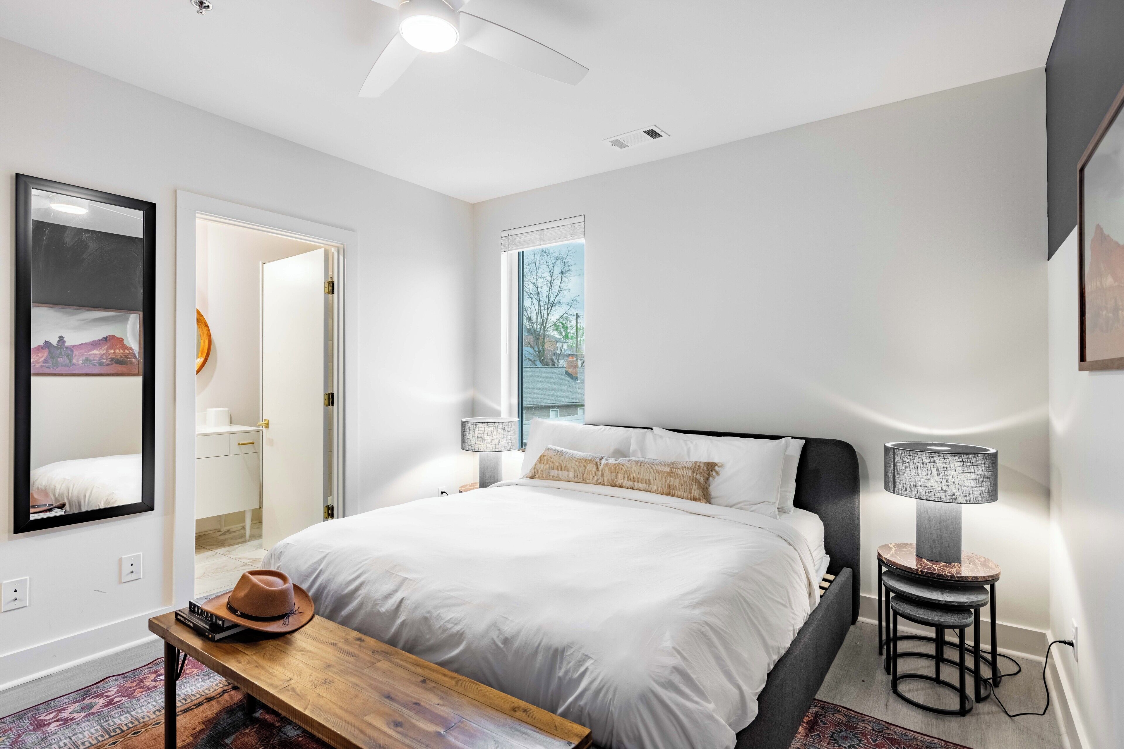 Un dormitorio moderno con una cama grande, lámparas de noche, una mesita de madera y un espejo en la pared.