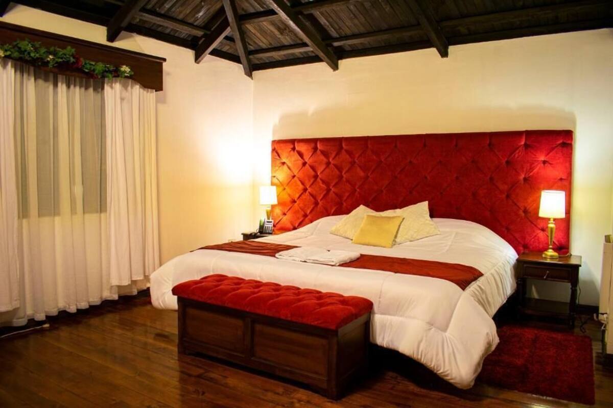 Een slaapkamer met een groot bed, een rode hoofdbord, witte beddengoed en een houten vloer, plus een rode bank.