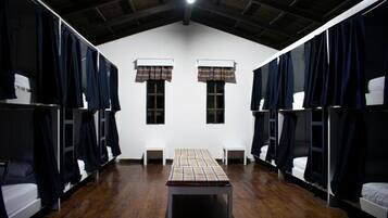 Una habitación con literas, una mesa central y dos ventanas con cortinas a cuadros.