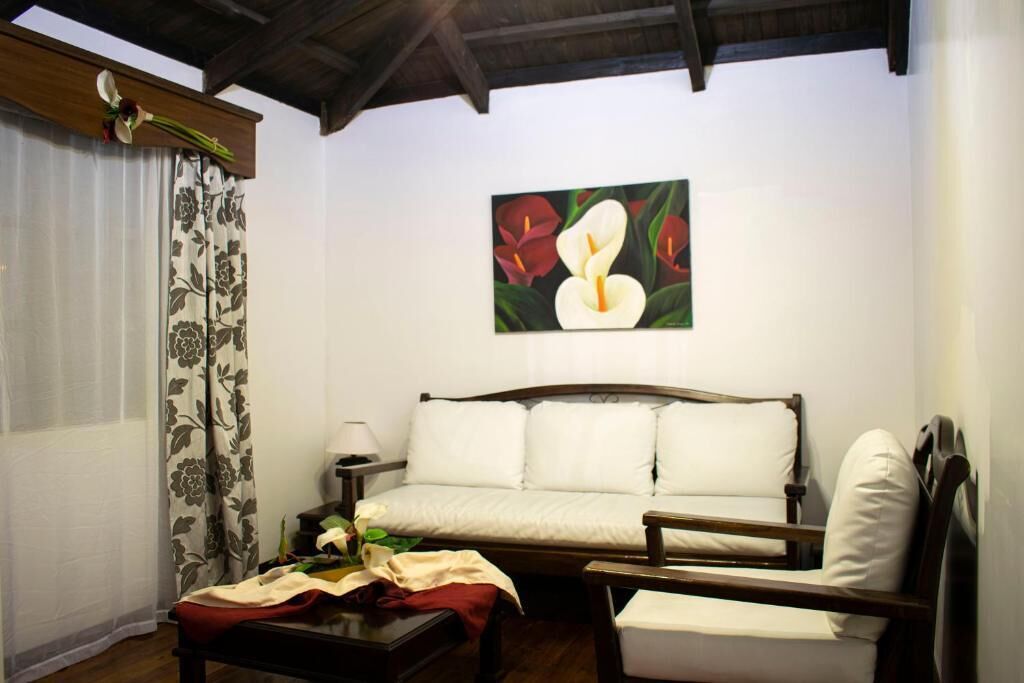 Una habitación con un sofá blanco, una silla de madera, una mesita pequeña y un cuadro de flores en la pared.