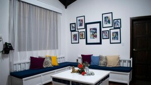 Une pièce avec un banc blanc servant de coin salon, une table basse blanche agrémentée d’objets décoratifs et des œuvres d’art encadrées accrochées au mur.