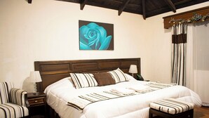 Une chambre à coucher bien aménagée, avec un grand lit, une table de chevet avec une lampe, une chaise et une œuvre d’art représentant une rose bleue, accrochée au mur.