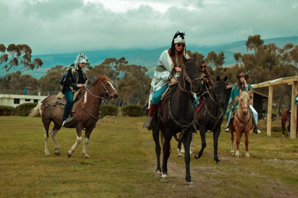 Un grupo de personas montando a caballo sobre un campo cubierto de hierba, con una estructura de madera al fondo.