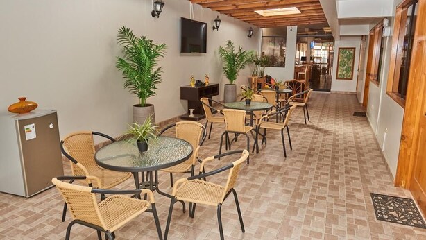 Amplio espacio interior con varias mesas redondas y sillas de mimbre, rodeado de plantas en macetas.