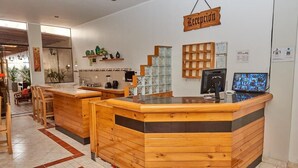 Zona de recepción con mostrador de madera, una pantalla de televisión y un cartel que dice 'Reception'.