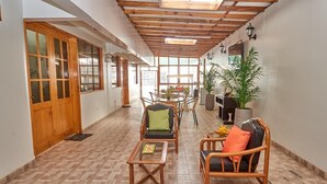 Un pasillo con techo de madera, suelo de baldosas y una zona de comedor con sillas y mesa.