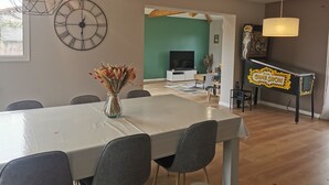 Ein Essbereich mit einem weißen Tisch, grauen Stühlen, einer Uhr und einer Vase mit getrockneten Blumen.