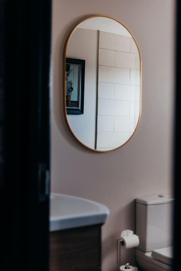 Une salle de bain avec un miroir rond, des carreaux blancs, des toilettes et un lavabo.