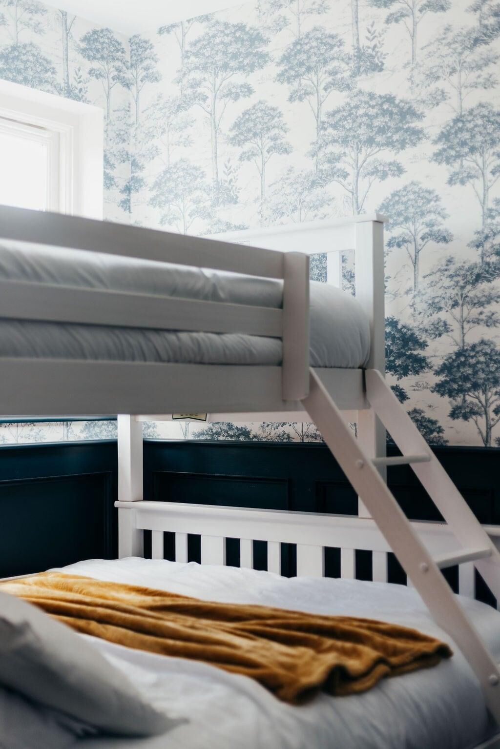 A bunk bed with a white frame and a view of a forest wallpaper.