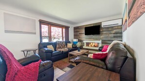 Una sala de estar moderna con chimenea, sofás de cuero, una mesa de centro y un televisor de pantalla plana montado en una pared de madera.