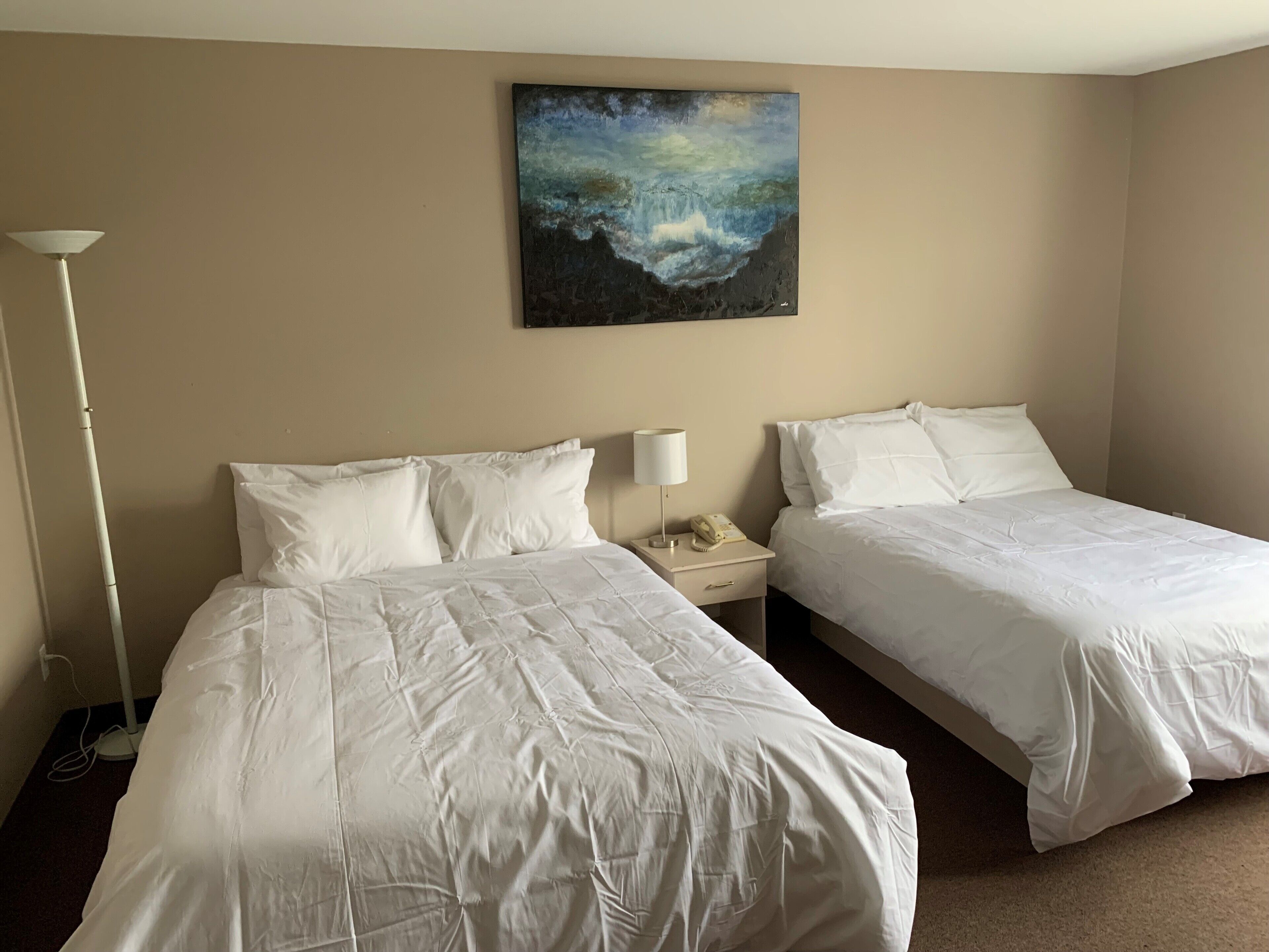 A hotel room with two beds, a nightstand with a lamp, and a painting on the wall.