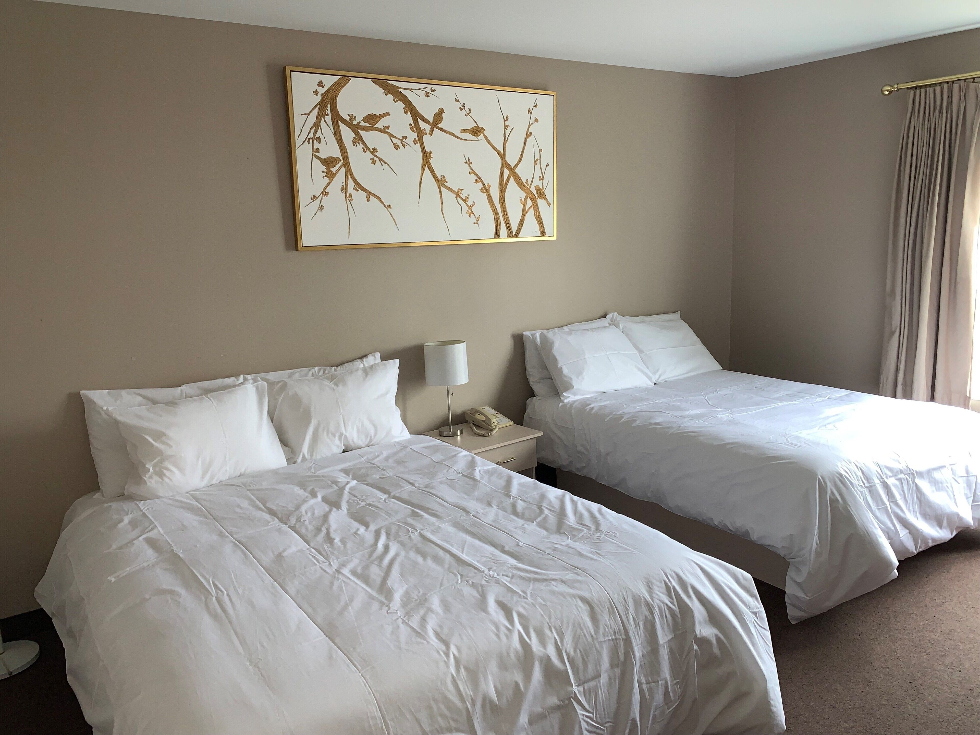 A hotel room with two beds, a bedside table with a lamp, and a wall-mounted artwork.