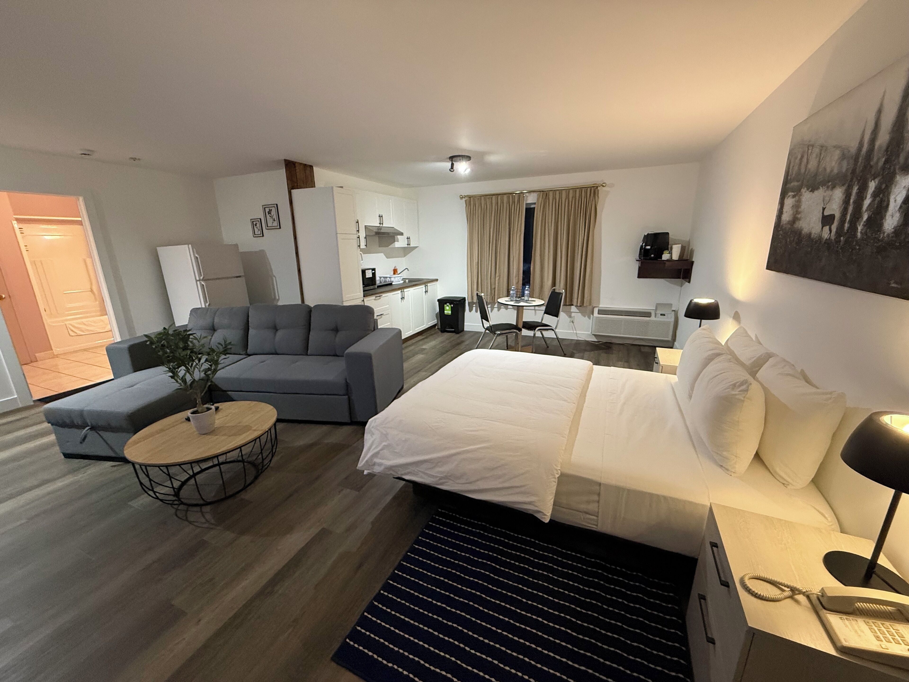 Una habitación de hotel moderna con cama, sofá, mesa de comedor y kitchenette.